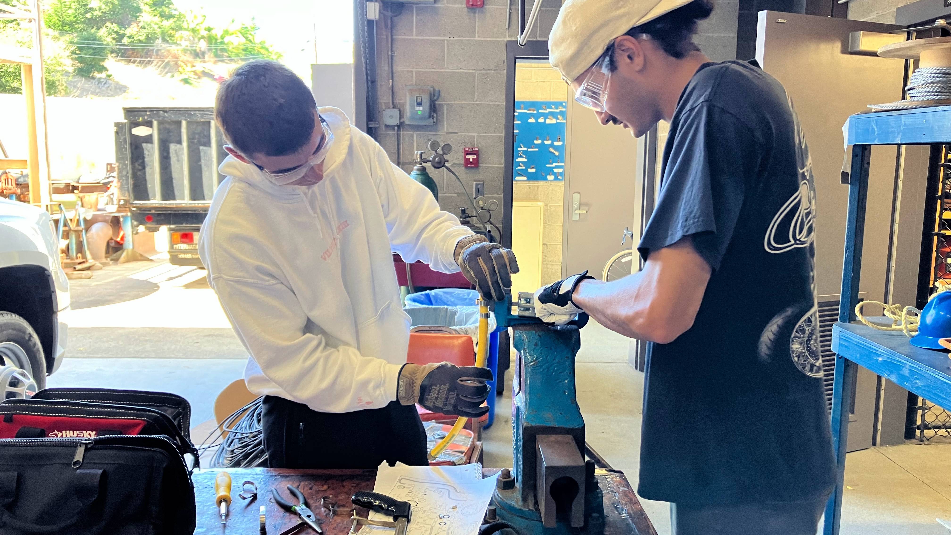 two students work together to put bandit clamps on a hose